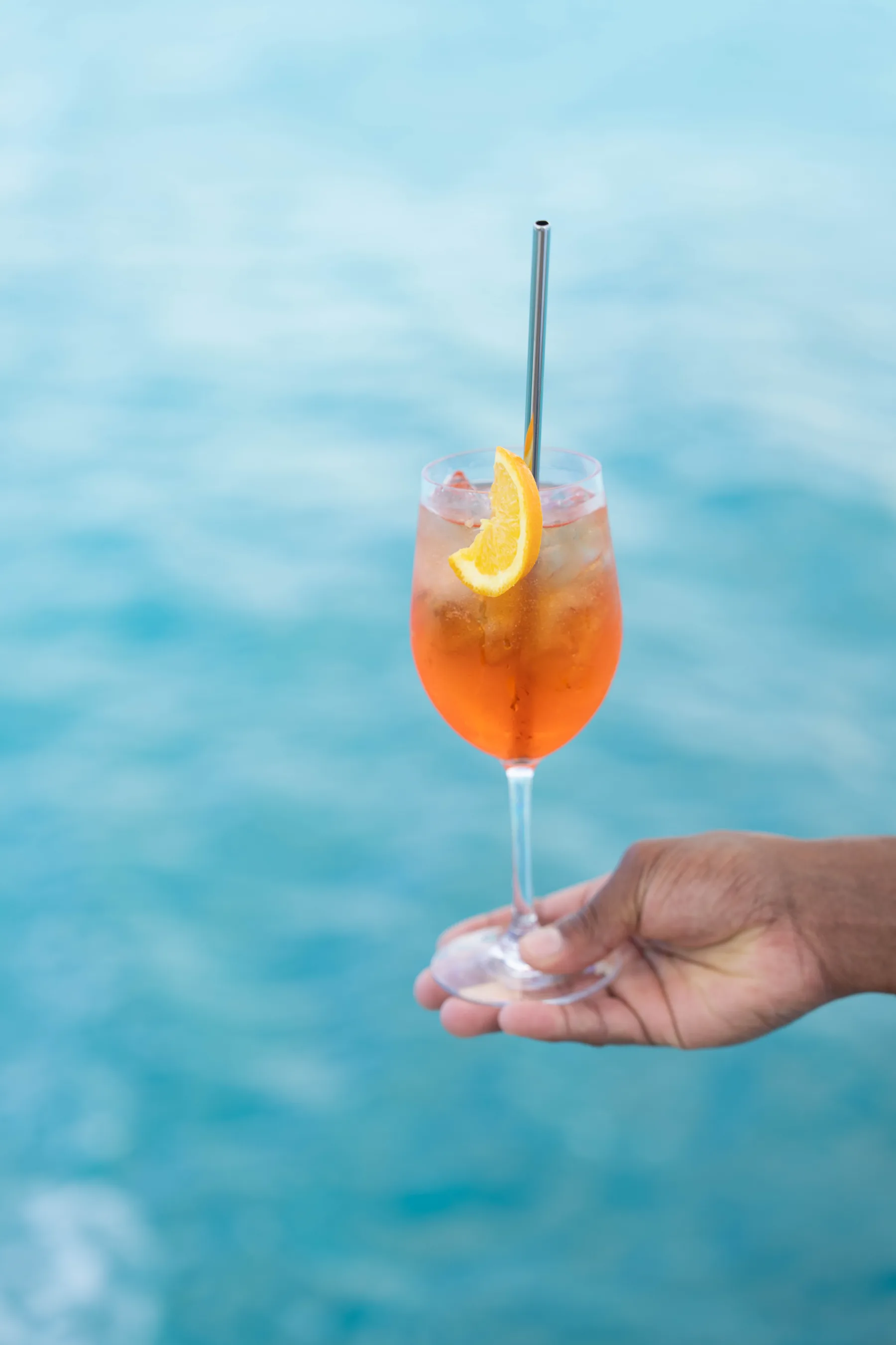 Aperol spritz held over turquoise water